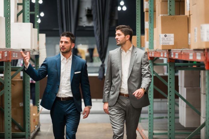 two business men in blue and grey suits walking through warehouse