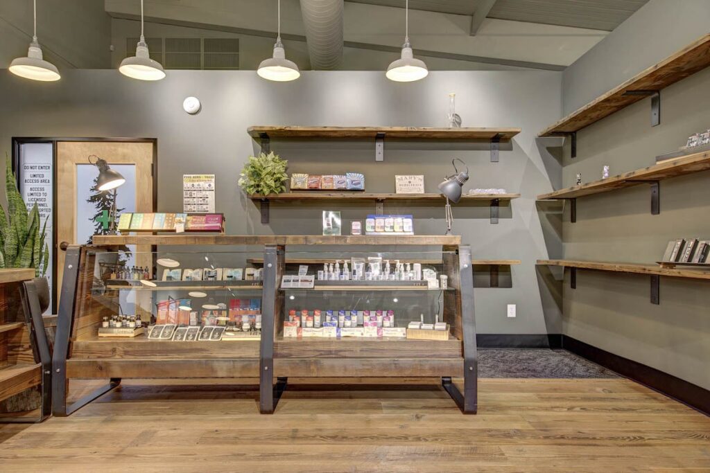 dispensary interior lights hanging from ceiling glass display case and wood floor with wood floating shelves on the wall