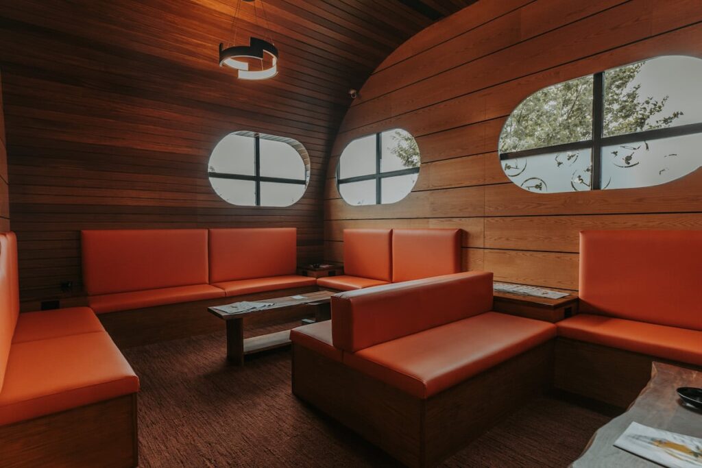 lounge with low warm lighting orange bench seating and oval windows 