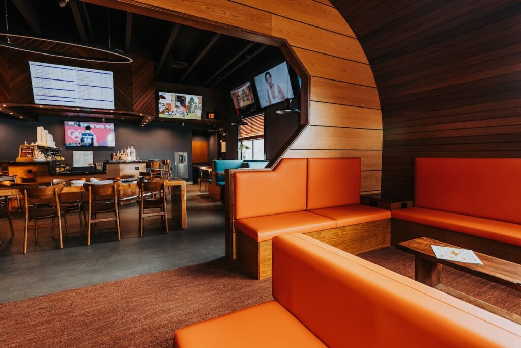 lounge cafe with wood walls, orange seating, and a bar with tvs on thee wall