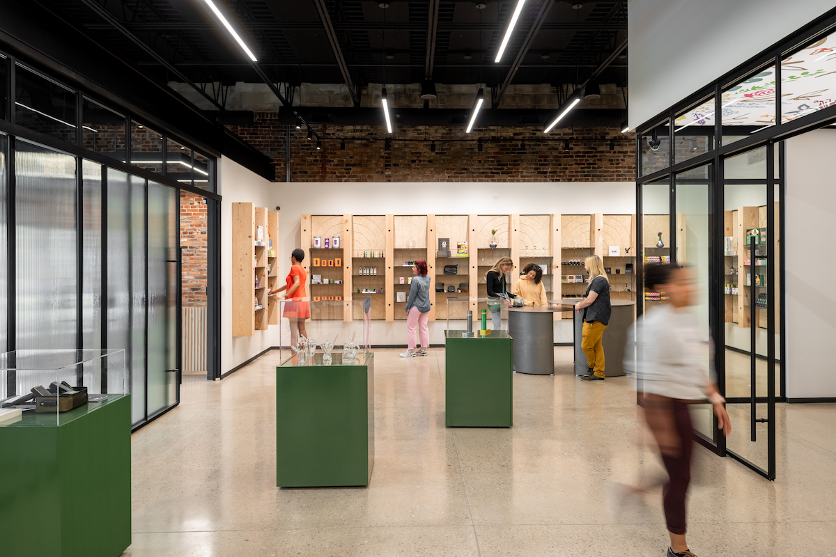 dispensary interior with wood floors and black ceilings and green display tables throughout the room