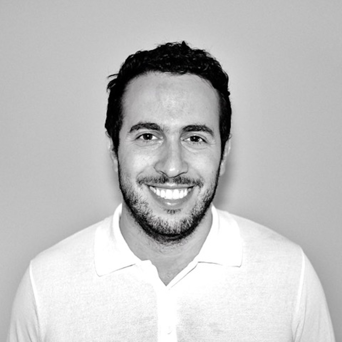 black and white headshot of a man with dark hair and facial hair smiling 