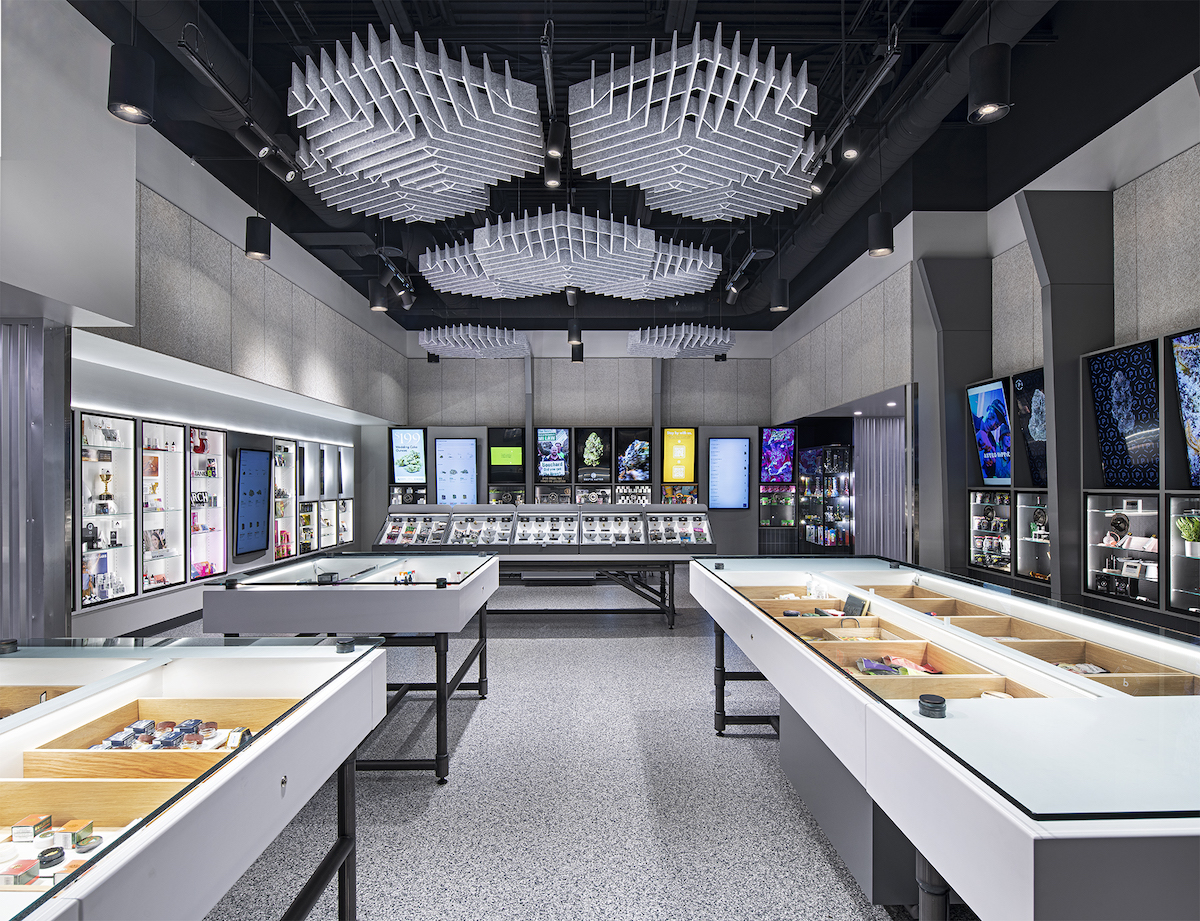 inside pure options dispensary gray floors high ceilings with white geometric 3D designs with white display tables and touch screens on the back wall