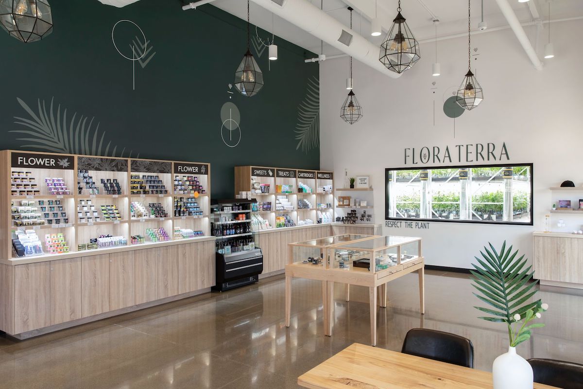 dispensary interior with shiny brown floors and a dark green accent wall flora terra is printed on an adjacent white wall and beneath it is a window into the grow room
