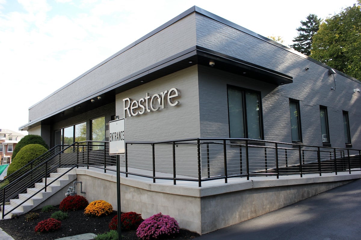 outside of restore dispensary gray rectangular building surrounded by brightly colored bushes