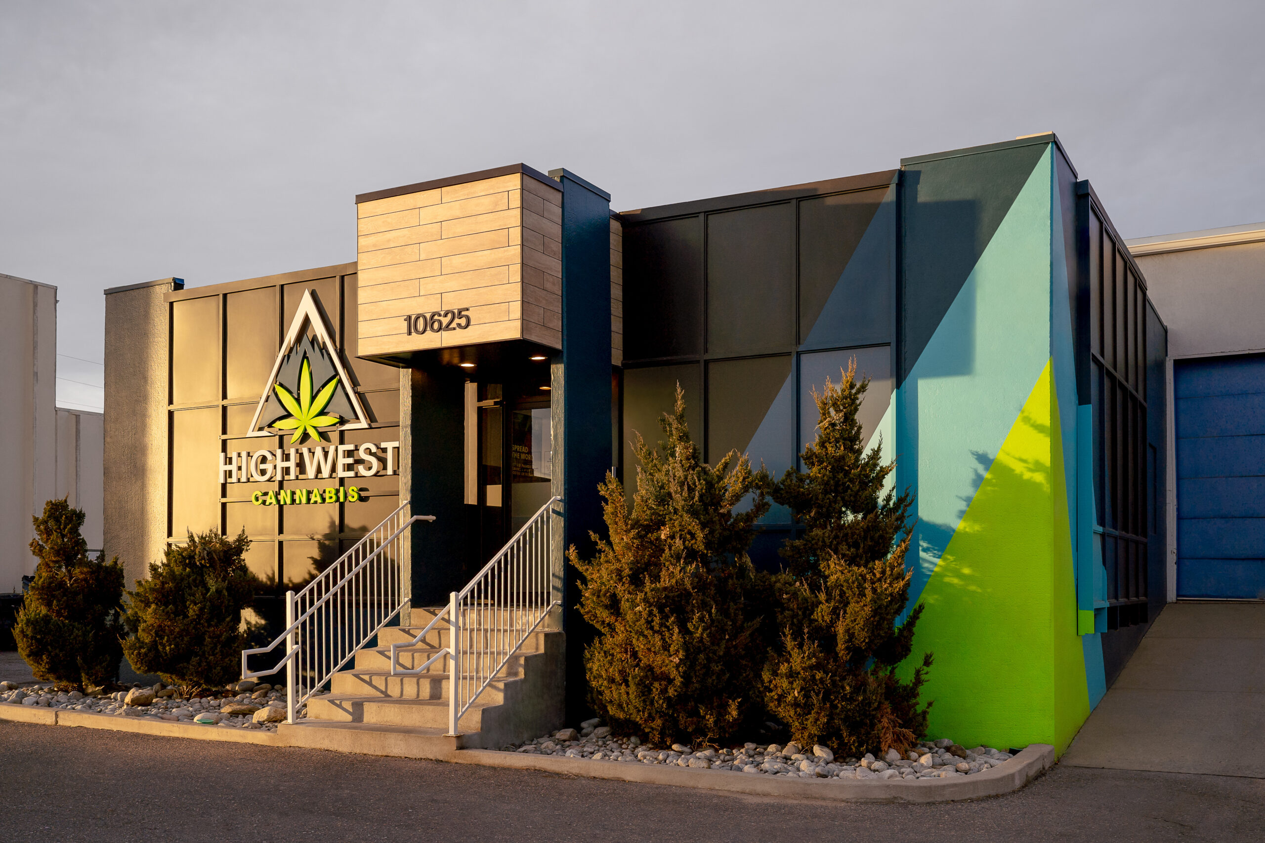 outside a rectangular dispensary building with pine trees in the front and a staircase leading inside